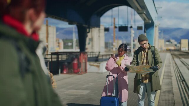 A young couple of tourists consults a map and phone on a city train platform. They navigate their urban journey, planning their next travel move.