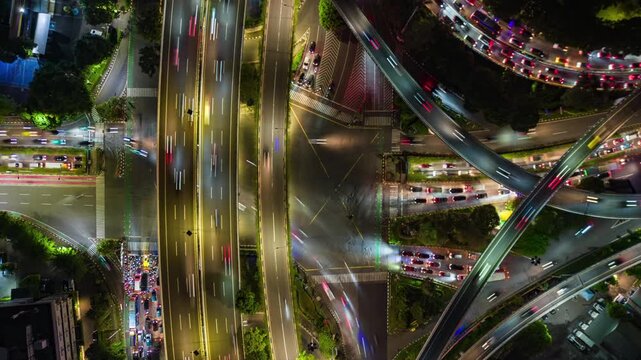 Night timelapse aerial view of busy highway interchange in Jakarta, Indonesia. Light trails from cars, multilayer roads, and urban traffic system in motion.
