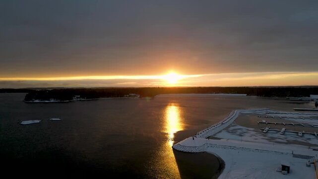 Aerial drone footage of winter in Vuosaari, Helsinki, Finland, as sunlight breaks through cloudy skies. Snow-covered landscape with dramatic lighting, coastal scenery, and a calm Nordic atmosphere.