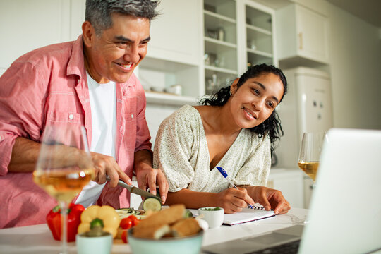 Smiling couple cooking together at home kitchen while following online recipe