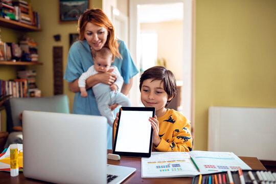 Mother with baby helping son learn online at home