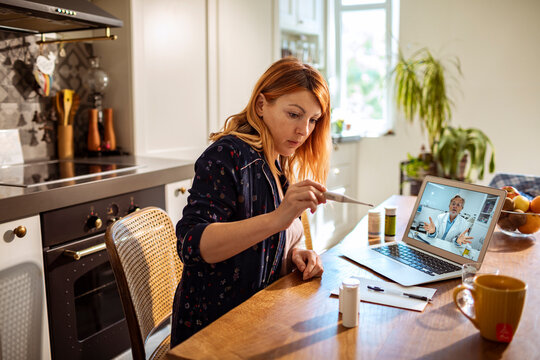Woman checks thermometer during telehealth consultation in home kitchen