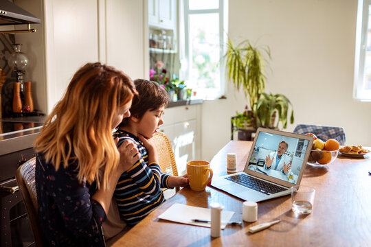 Mother and child consulting pediatrician via telehealth in home kitchen