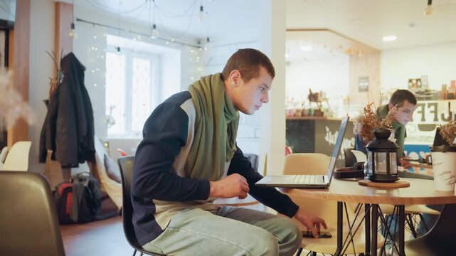White man juggling phone and laptop remote worker switching between scrolling, checking watch and urgent typing, intermittent sipping from mug, visible impatience, backpack and coat hung nearby, warm