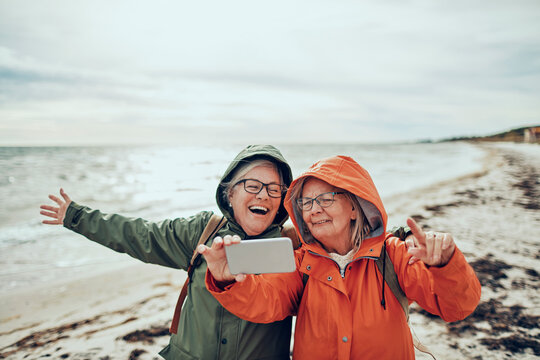 Two senior women taking a selfie on a windy beach