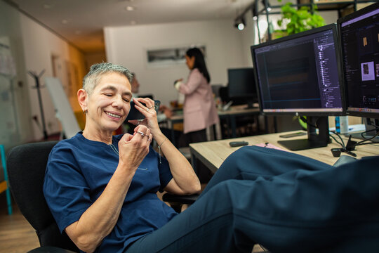 Smiling mature designer taking phone call at modern office desk