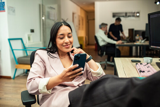 Smiling businesswoman relaxing with smartphone in modern office