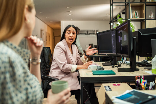 Businesswoman leading discussion with coworker at dual monitors in modern office