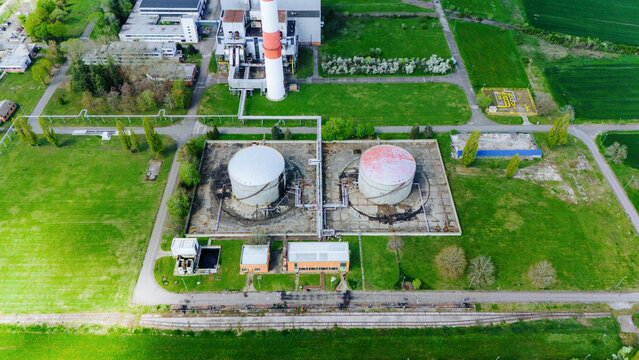 Aerial view of industrial tanks gleaming under the sun contrasting with the surrounding vibrant green fields and structures, Zrenjanin, Vojvodina, Serbia.