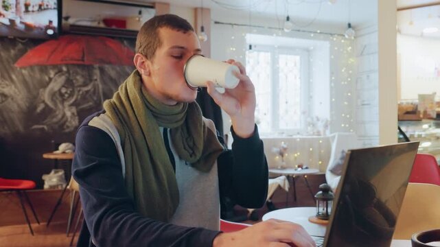 Caucasian man coding in bistro laptop coffee, evening light and warm interior, focused gaze while typing, green scarf and mug at side, steady workflow during late session, startup energy and creative