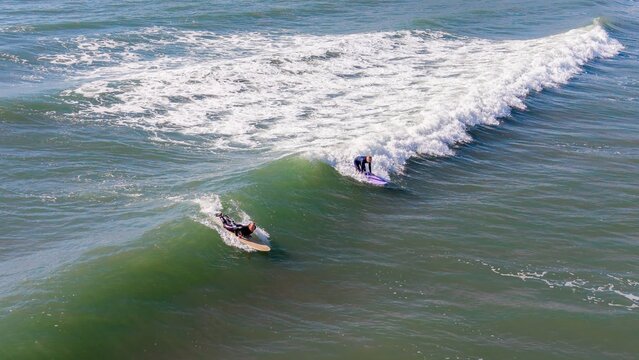 Aerial view of surfers riding the powerful, emerald waves as they curl and crest near Burgh Island, England, United Kingdom.