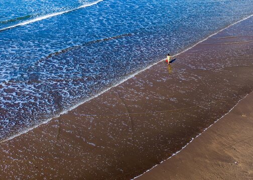 Aerial view of a young boy standing on the shore as the tide recedes, the dark sand contrasting with the bright sea, Burgh Island, England, United Kingdom.