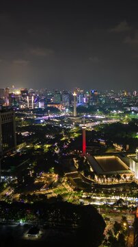 Aerial night view of Jakarta featuring National Monument Monas and Istiqlal Mosque illuminated among city lights. Modern urban skyline and iconic landmarks in Indonesia.