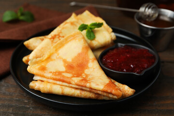 Tasty crepes with mint leaves and jam served on wooden table, closeup © New Africa