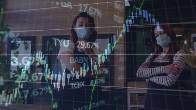 Two female coworkers standing inside cafe wearing dark aprons and masks, monitoring stock charts