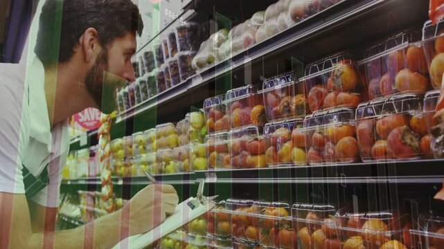 Mid adult man in apron checking peaches in produce aisle, using pen on clipboard, copy space