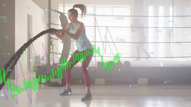 Woman using battle ropes and doing alternating waves in fitness gym, waveform tracking effort