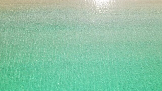 Shallow turquoise sea water lapping onto white pebble shore of secluded beach