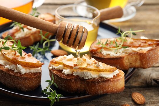 Dripping honey onto delicious bruschettas with cream cheese, pears, almonds and thyme at wooden table, closeup