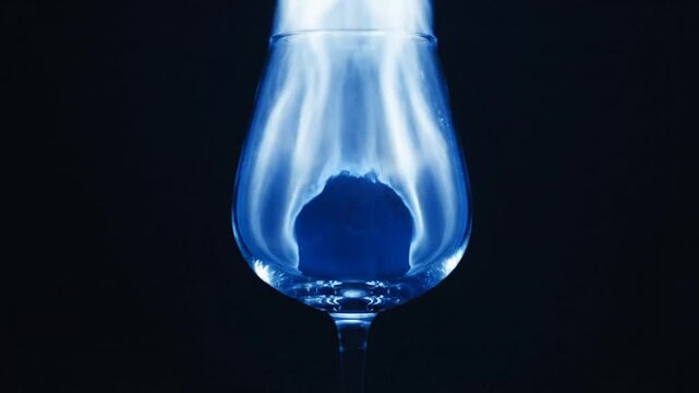 Blue fire burning inside a clear glass against black background