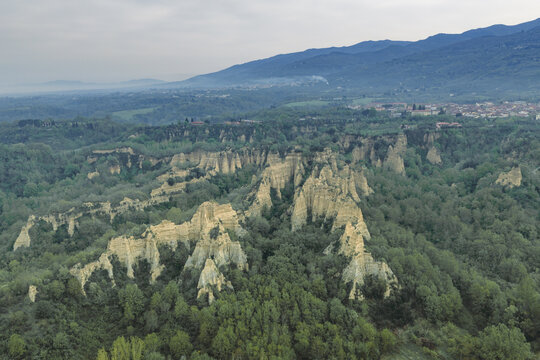Aerial view of the unique clay pinnacles of Le Balze del Valdarno surrounded by dense green forest and rolling hills under an overcast sky in Castelfranco Piandisco, Tuscany, Italy.