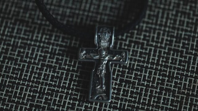 Close-up of a silver cross pendant hanging from a black leather necklace
