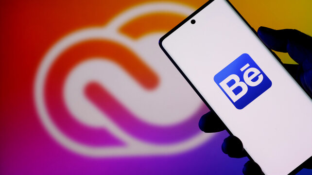 Hand holding a smartphone displaying the behance logo against a colorful background