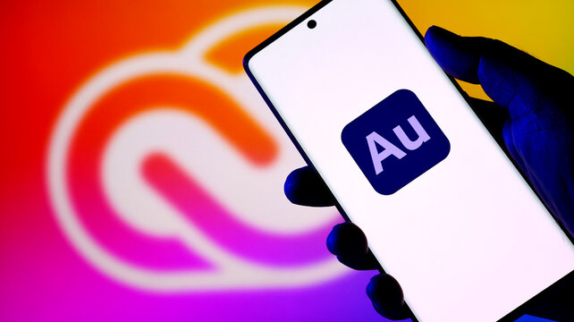 Hand holding a smartphone displaying the adobe audition app icon