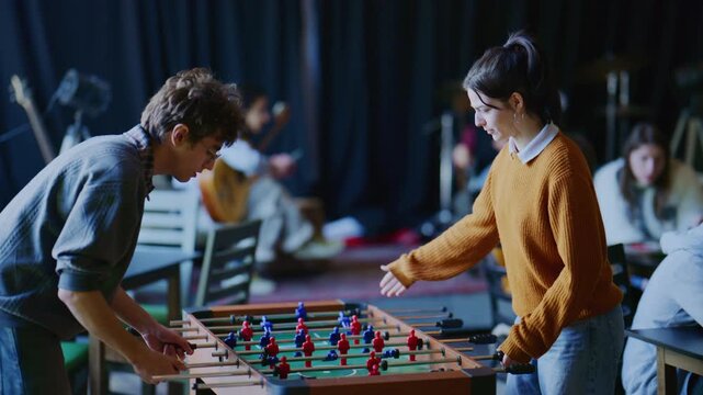 Two young students are seen playing a competitive game of foosball, enjoying their leisure time. They share a moment of high-five celebration after scoring a goal.