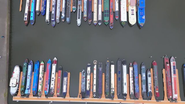 Aerial top down pan view of 2 rows of canal barges or boats moored in a marina.