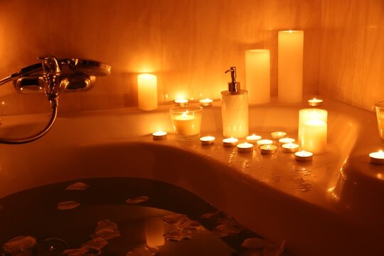 Romantic atmosphere. Bathtub with burning candles, petals and soap in bathroom, closeup