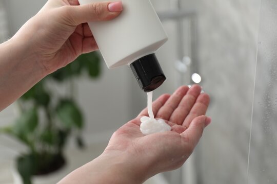 Woman pouring shampoo onto hand in bathroom, closeup