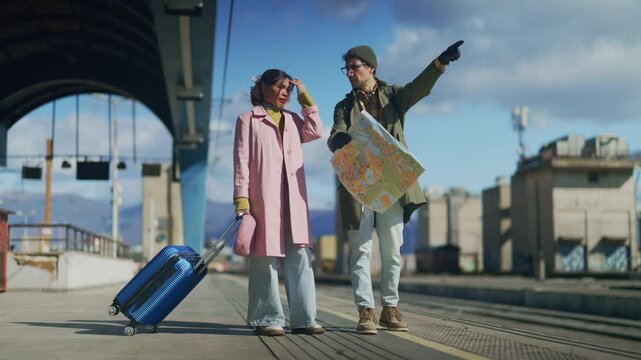 Two tourists consult a map while standing on a city train station platform. The traveling couple appears to be navigating their journey through the urban environment.