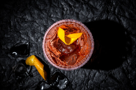 Negroni cocktail on black leather background. Italian IBA drink with gin, vermouth and orange. Fresh stir with ice. Classic alcoholic beverage at the bar in harsh light. Luxury, rich taste. Close up