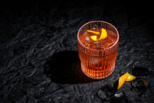 Negroni cocktail on black leather background. Italian IBA drink with gin, vermouth and orange. Fresh stir with ice. Classic alcoholic beverage at the bar in harsh light. Luxury, rich taste. Close up