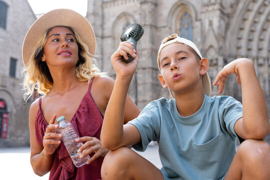 Family tourists combating summer heat in the Gothic Quarter, staying cool with a mini fan and bottled water