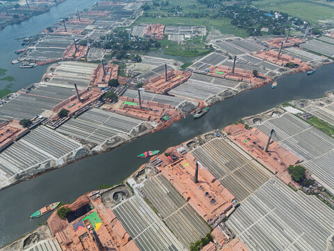 Aerial view of numerous brick kilns with tall chimneys and rows of drying bricks along a river canal Narayanganj, Dhaka Division, Bangladesh.