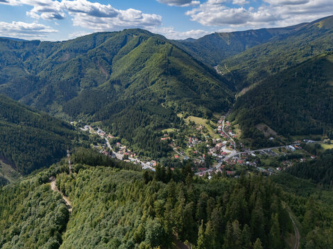 Aerial view of the village of Stare Hory nestled in a lush green valley surrounded by forested mountains under a blue sky with scattered clouds Stare Hory, Banska Bystrica Region, Slovakia.