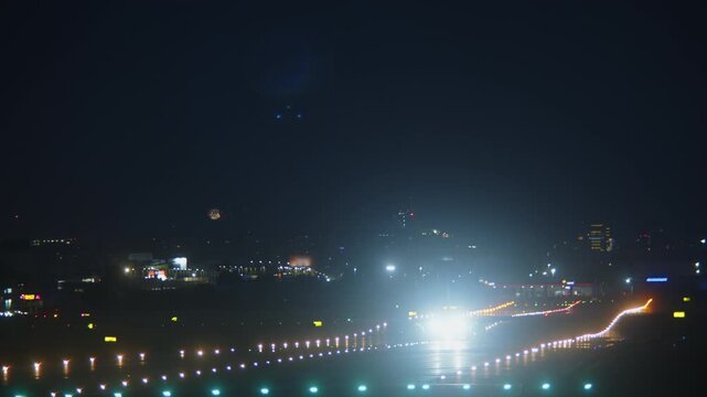 Aircraft taxiing on illuminated runway at night with fireworks explosion bursting in sky above city lights in background, airport runway lights glowing in darkness