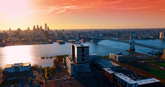 Beautiful pink sky with light feathery clouds over the cityscape of Philadelphia, Pennsylvania, USA. Drone footage descending over the waterfront of the Delaware River at sunset.