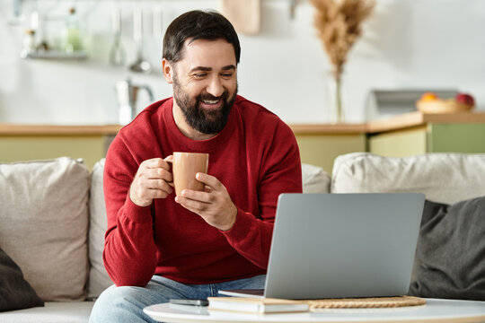 Handsome man enjoying a warm drink while working on his laptop at home in the cozy living room