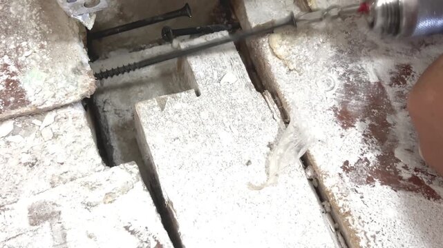 Worker applies expanding foam insulation in a wall gap indoors. construction repair, home renovation, insulation work.
