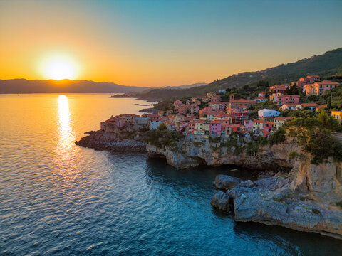 Aerial view of the colorful coastal village perched on rocky cliffs during a vibrant sunset over the Mediterranean Sea Tellaro, Liguria, Italy.