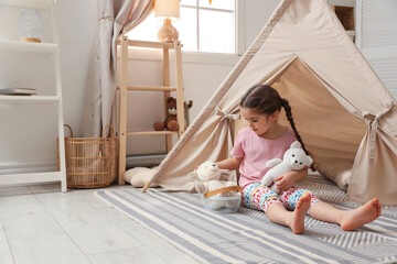 Little girl playing with toys near toy wigwam in playroom, space for text © New Africa