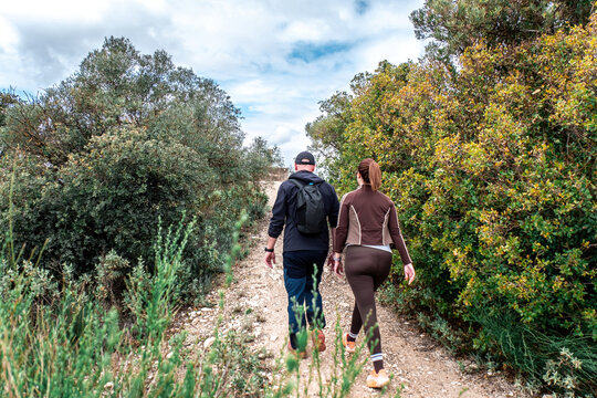 Couple hiking uphill on a narrow green trail, back view, enjoying an active outdoor adventure in sunny, leafy mountain scenery