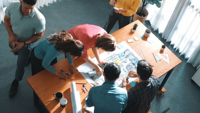 Top view of smart manager writing at blueprint while marketing team plans design. Aerial view of architect engineer working together sharing idea and taking a note in project plan at table. Symposium.