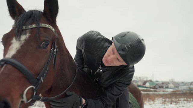 White coach adjusting horse bridle closely, handson tandem education on snowy field, helmeted caucasian rider receiving instruction, leather reins and saddle visible, focused expression