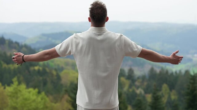  Young man standing with open arms facing the misty mountains forest.