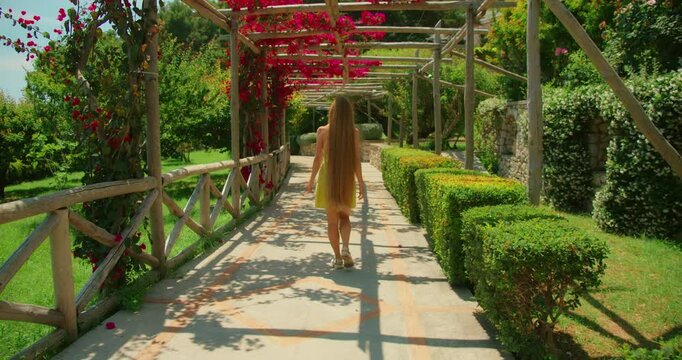 Young woman walking through a wooden garden pergola with bright flowers in summer