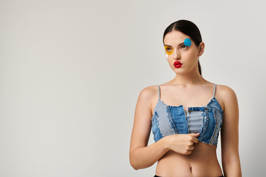Young woman showcases vibrant face art with stylish denim outfit in a creative setting